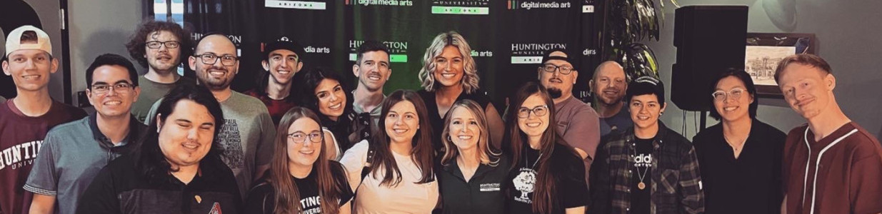 A group of 18 HU Arizona Alumni are smiling at the camera at an event with speakers in the background.