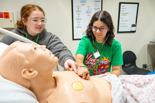 Two summer nursing students practice on a medical dummy.