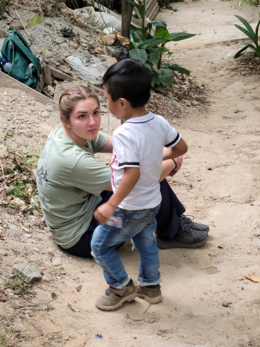 A picture of an HU student sitting on the ground while speaking to a child on an international missions trip.