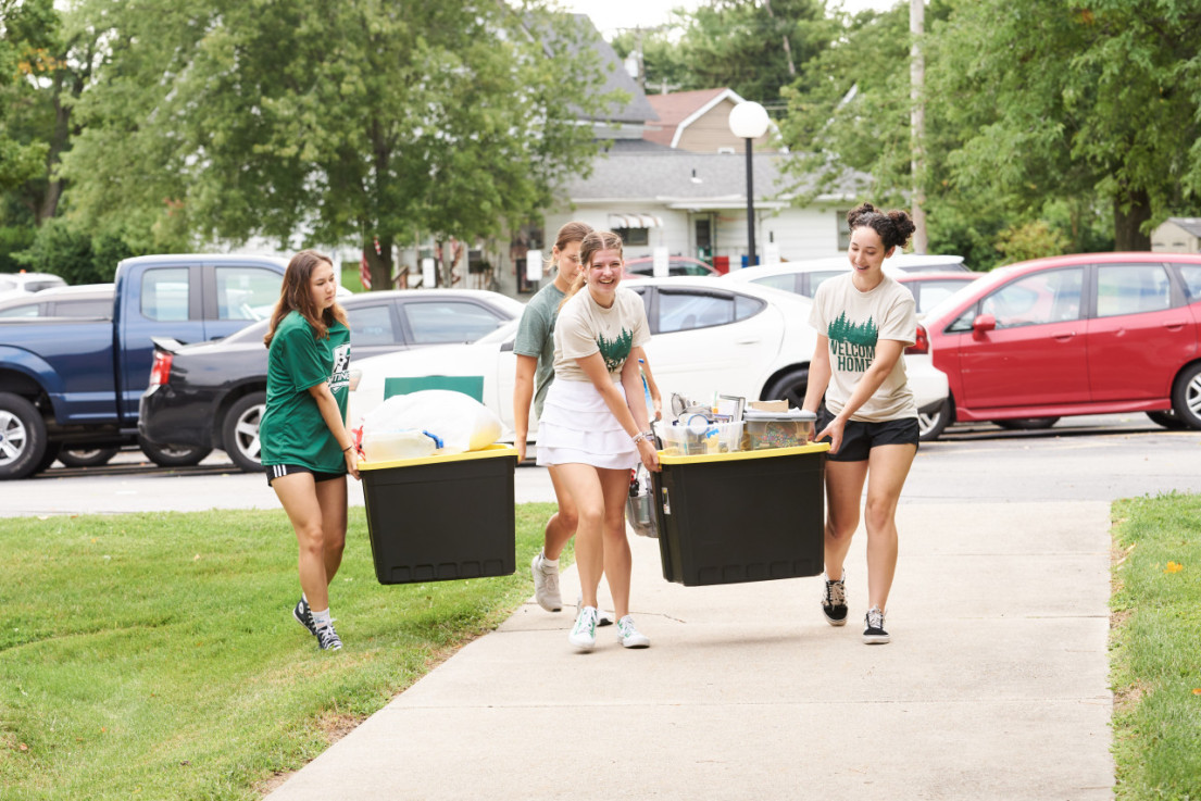 Female students carry tubs full of supplies into a residence hall during move-in day in 2023